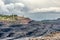 A large quarry with many horizons and ledges. Vertical bedding of coal seams.