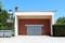 Large red bricks garage with elongated garage doors made from narrow wooden boards with faded color next to small storage silo