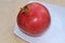 Large red bright pomegranate. On a white glossy plate