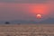 Large red circle of sun in a haze sets behind the silhouette of the mountains and clouds on the