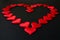 A large red heart, laid out of many small identical red silk hearts, on a black background. A symbol of love and passion