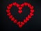 A large red heart, laid out of many small identical red silk hearts, on a black background. A symbol of love and passion