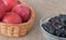 Large red plums in a wicker basket and prunes in a glass cup on
