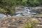 Large rocks making up riverbed with low water level surrounded by green trees