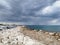 Large rocks on the shores of the Mediterranean Sea, dramatic skies and rain over the largest sailing yacht in the world, an eight-