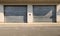 Large roller shutter garage doors on a concrete facade with a no stopping sign in the middle. Cement sidewalk and road.