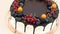 A large round cake is decorated with fresh berries. Vertical wiring