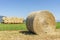 A large round hay bale in a field in the Tuscan countryside, with a trailer full of hay bales in the background, Italy