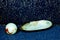 A large shell, mother of pearl, and a light marble in front of a blue and golden background, shimmering like stars in the universe