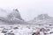 a large snow covered mountain with low clouds and rocks in the foreground