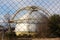 Large sphere storage structure with metal steps on one side surrounded with dried grass and trees in front of dense wire fence