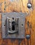 Large square rusty iron lock with keyhole in an old varnished wooden door with the end of the key visible and metal rivets