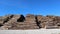 Large stack of chopped tree trunks under the sun, between a country road and the blue sky