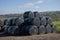 Large stack of haylage bales wrapped in black plastic, sunny rural day