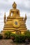 A large statue of a gilded sitting Buddha on a background of clouds.