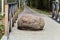 A large stone lies in the middle of a wooden bridge. Against the background of the forest and the river