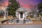 a large stone mausoleum in the graveyard with bare winter trees and lush green trees and powerful clouds at sunset