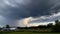 a large storm cloud looms over a farm in the distance