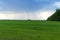 A large storm cloud over a wide green agricultural field. In the distance it rains.