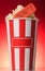 Large striped popcorn box with orange ticket to the movies on red background