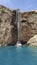 A large strong waterfall falls from a rocky precipitous shore into the blue Mediterranean Sea