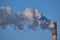 Large tall brick old pipe CHP strongly smokes against a blue clear sky