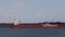 Large tanker ship moored at a river port with mind turbine behind it