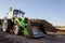 A large tractor with a bucket stands next to a pile of garbage. production waste recycling. Clear blue sky on a sunny day