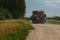 A large tractor carries dry hay rolls along a country road