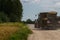 A large tractor carries dry hay rolls along a country road