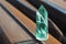 Large transparent mystical faceted crystal of colored green emerald quartz on a rails on industrial background close-up.