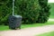 Large trash container in a city park. Green plastic trash can standing near trees