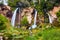 Large triple waterfalls over cliffs in lush green forest landscape