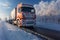 A large truck driving down a snow covered road during the winter. Sunset