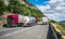 Large trucks carrying different products, on a beautiful mountain road, on a summer day. Near the road is a beautiful river, the