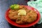 Large Viennese schnitzel on a red plate with lemon on a black background.