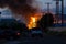 Large warehouse fire in the distance beyond spectators sitting in their cars shallow depth of field and focus