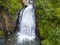 A large waterfall in the back of the Altai Mountains with gray-brown stones near a steep cliff with green trees. Waterfalls Korbu