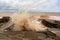 A large wave crashes into splashes on a breakwater during a storm