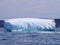 Large wave crashing against the side of a jagged iceberg