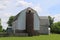 A large white farm barn and stone foundation and silo with green grass lawn and trees