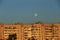 Large white full moon on clear blue over an urban city high building