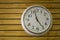 Large white round clock close-up with arrows on a yellow wooden plank wall. horizontal lines. natural texture surface