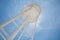 A large white water tower from below backlit by the sun with a bright blue sky.