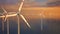 Large wind turbines with blades in field aerial view bright orange sunset blue sky wind park slow motion drone turn. Silhouettes