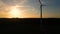 Large wind turbines with blades in field aerial view bright orange sunset blue sky wind park slow motion drone turn. Silhouettes