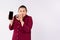 Large woman eating candies, holding mock up smartphone screen to camera. Silence gesture, hush, secret expression on