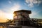 A large wooden beach pavilion, with a sun burst causing light rays as the sun sets behind the building.