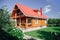 Large wooden newly built country house with red tile roof, lawn area on right and cherry trees orchard behind house and