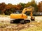 Large yellow backhoe with tracks sitting in vacant lot in leafy residential area with nice swingset and house in background